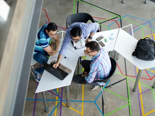 Three men collaborating over a laptop in a modern, geometric-themed office space.